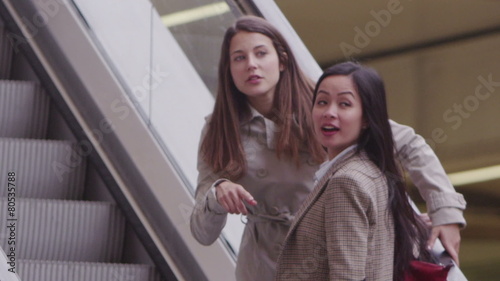 2 young female friends chat as they ride the escalator