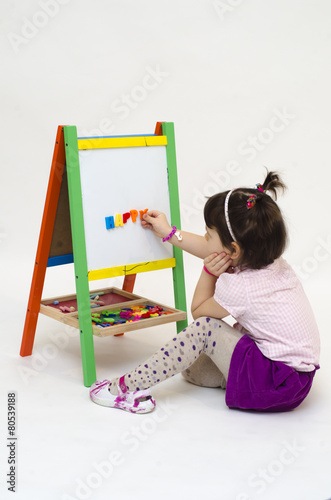 Musingly girl glues magnetic letters on white board isolated photo