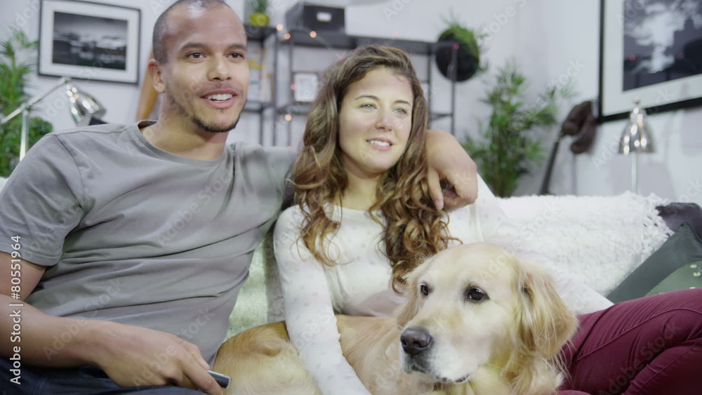 Attractive young couple watching television at home with their dog as their companion. In slow motion. Attractive young couple watching television at home with their dog as their companion. In slow motion.