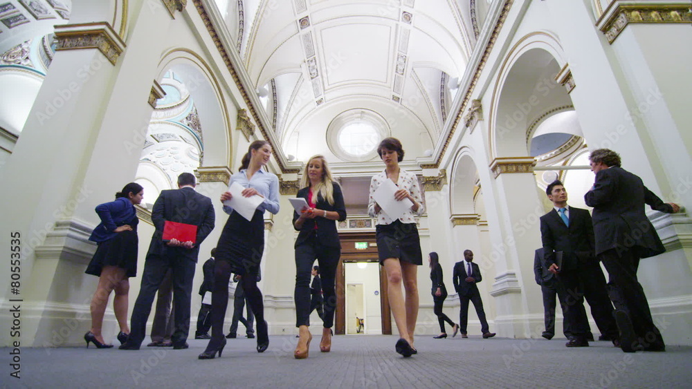Attractive female business delegates chat as they walk through elegant building Attractive female business delegates chat as they walk through elegant building