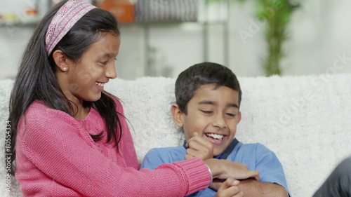 A young girl tickles her brother and they both laugh