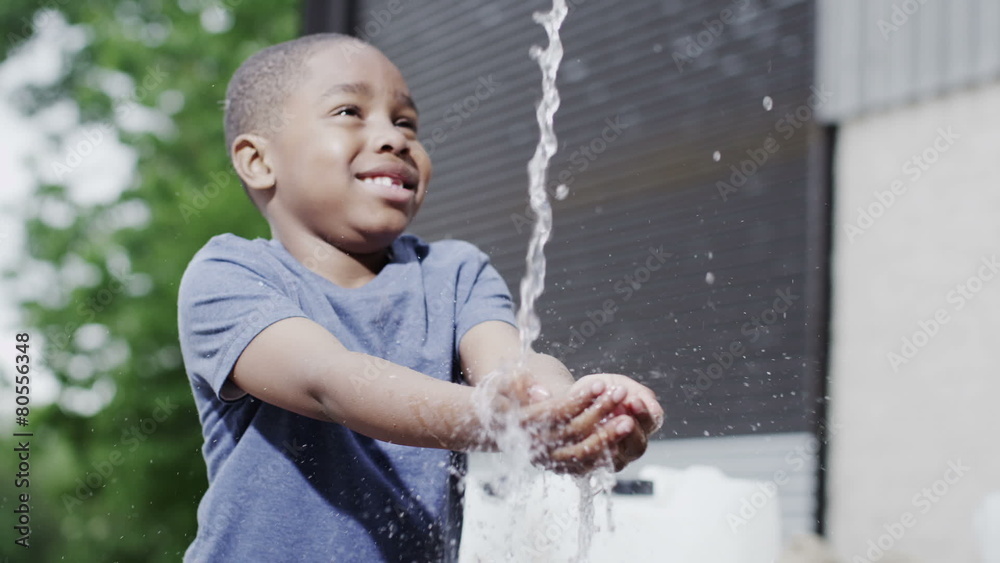 Happy, smiling African boy enjoys the sensation of fresh water on his hands