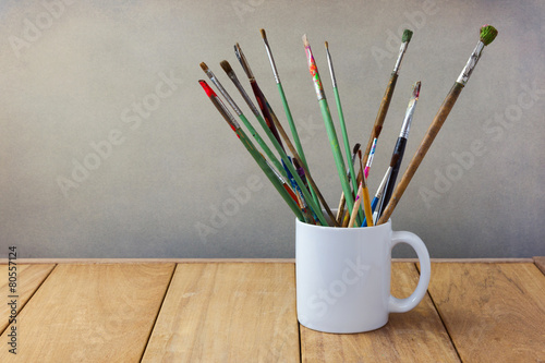 Painting brushes in white cup on wooden table