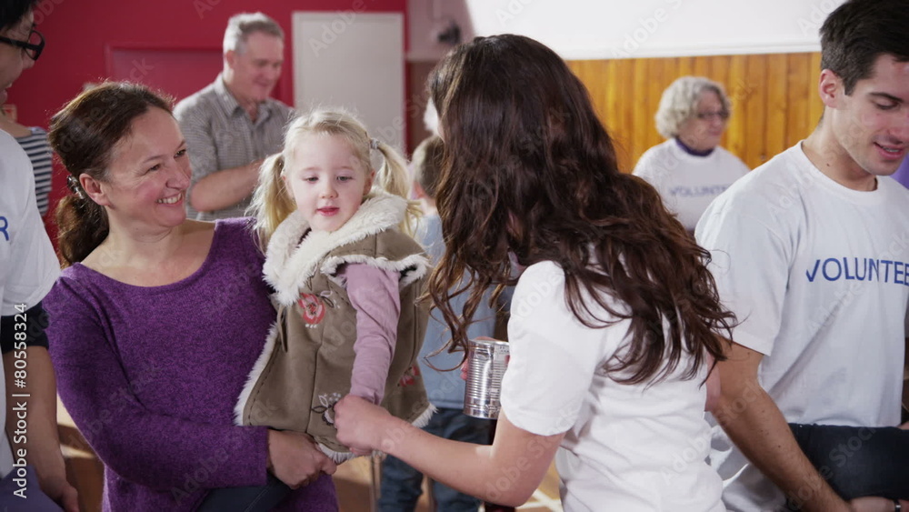 Beautiful charity worker accepts a can of food from cute little blonde girl Beautiful charity worker accepts a can of food from cute little blonde girl
