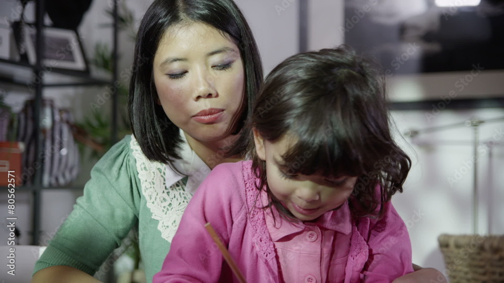 A loving mother is spending time with her small daughter in the evening, watching as she uses a variety of coloured pencils to write and draw. A loving mother is spending time with her small daughter in the evening, watching as she uses a variety of coloured pencils to write and draw.