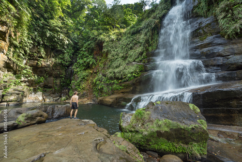 Man looking at huge jungle waterfall surrounded by lush greenery in the remote rainforest of Iriomote-jima, Okinawa, tropical Japan