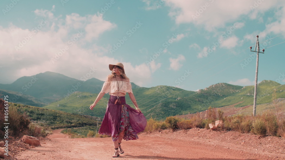 Rearview of boho girl walking down a country dirt road