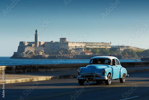 Old classic car on street of Havana with ocean and lighthouse in photo