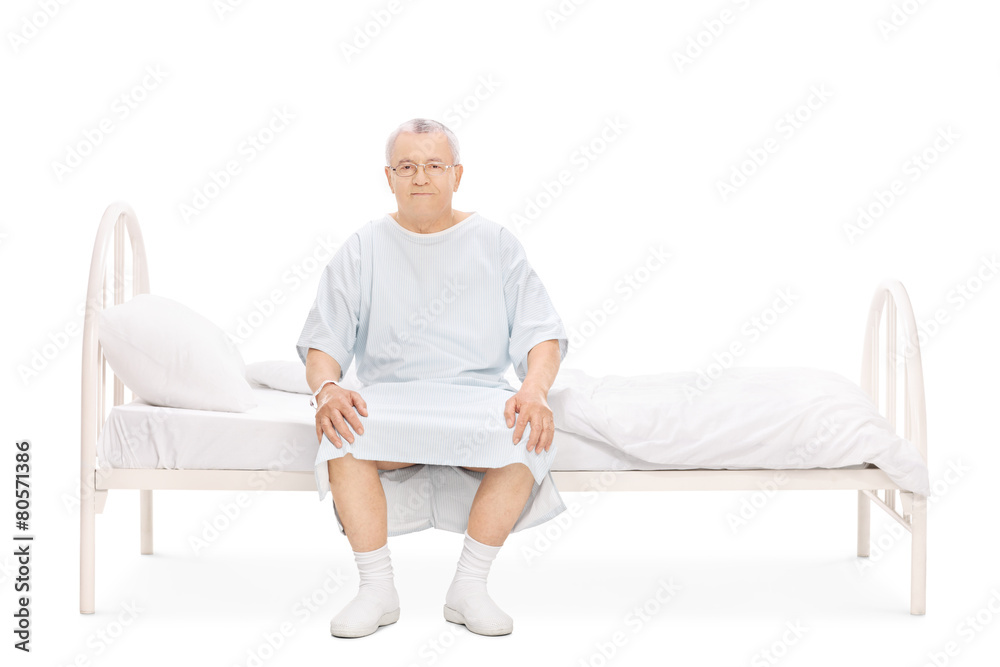 Mature patient in a hospital gown sitting on a bed