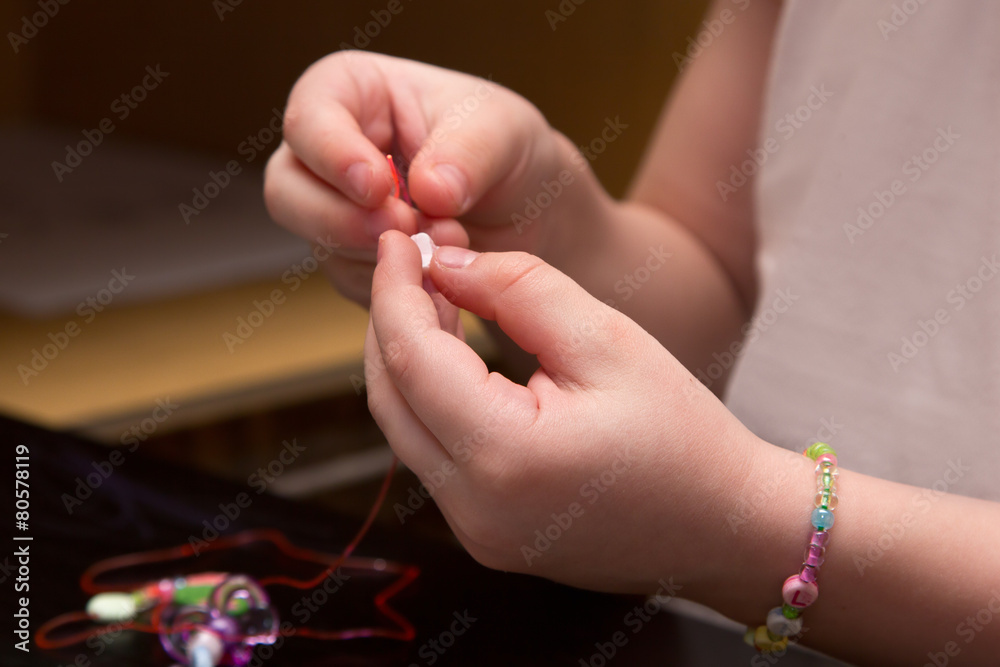 child's hands strung beads on thread