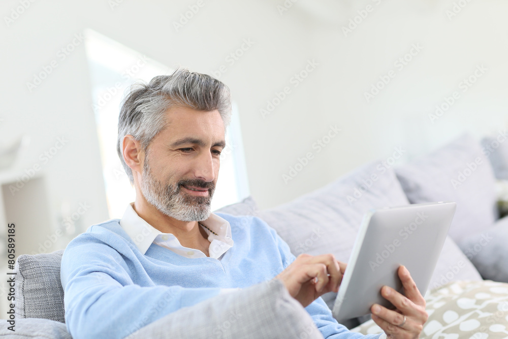 Mature handsome man websurfing on tablet at home Mature handsome man websurfing on tablet at home