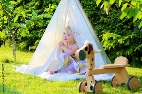 Preschooler girl playing in the garden hiding in tent
