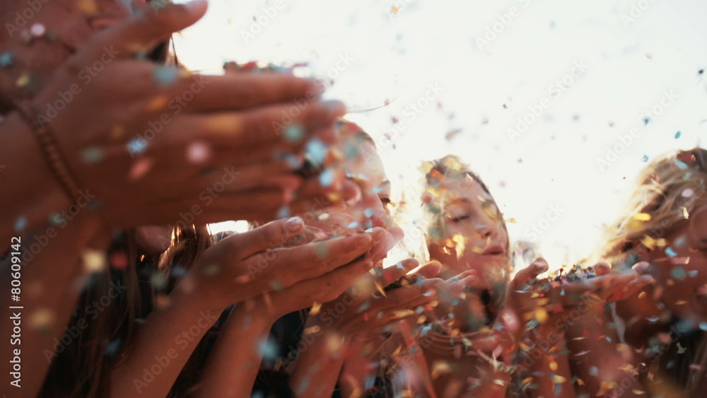 Teens blowing colorful confetti together outdoors with sun flare
