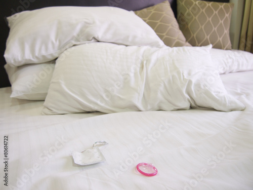 Messy bed in a hotel with a pink condom