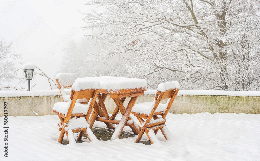 Wooden table with chairs covered in fresh snow after a winter bl