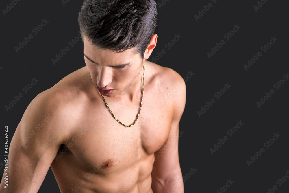 Handsome, fit young man shirtless, against dark background