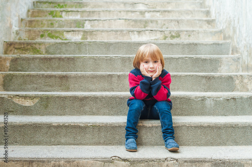 Adorable little boy with sitting on steps in a city