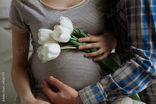 Fototapeta Naklejka Na Ścianę i Meble -  Young pregnant woman sitting with husband and holding flowers