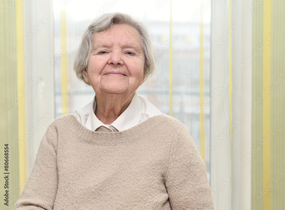 Senior happy woman in her home with window on background.