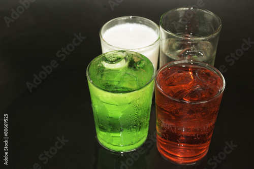 Red and green milk and ice in a glass on a black background.