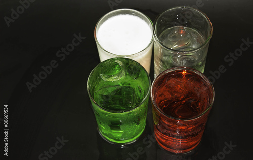 Red and green milk and ice in a glass on a black background.