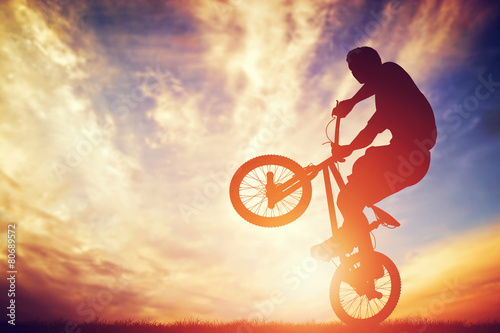 Fotografering Man riding a bmx bike performing a trick against sunset sky