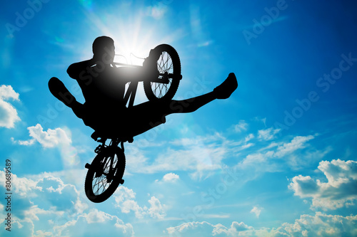 Billede på lærred Man jumping on bmx bike performing a trick against sunny sky