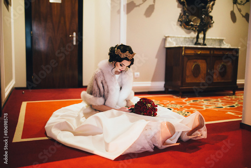 Beautiful bride sitting on the floor and holding a smartphone photo