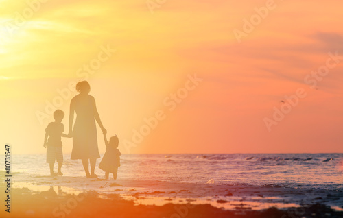 mother and two kids walking on the beach at sunset