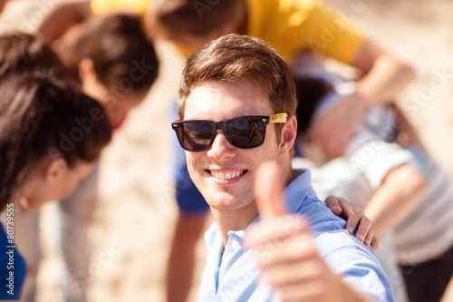 happy young man in sunglasses showing thumbs up