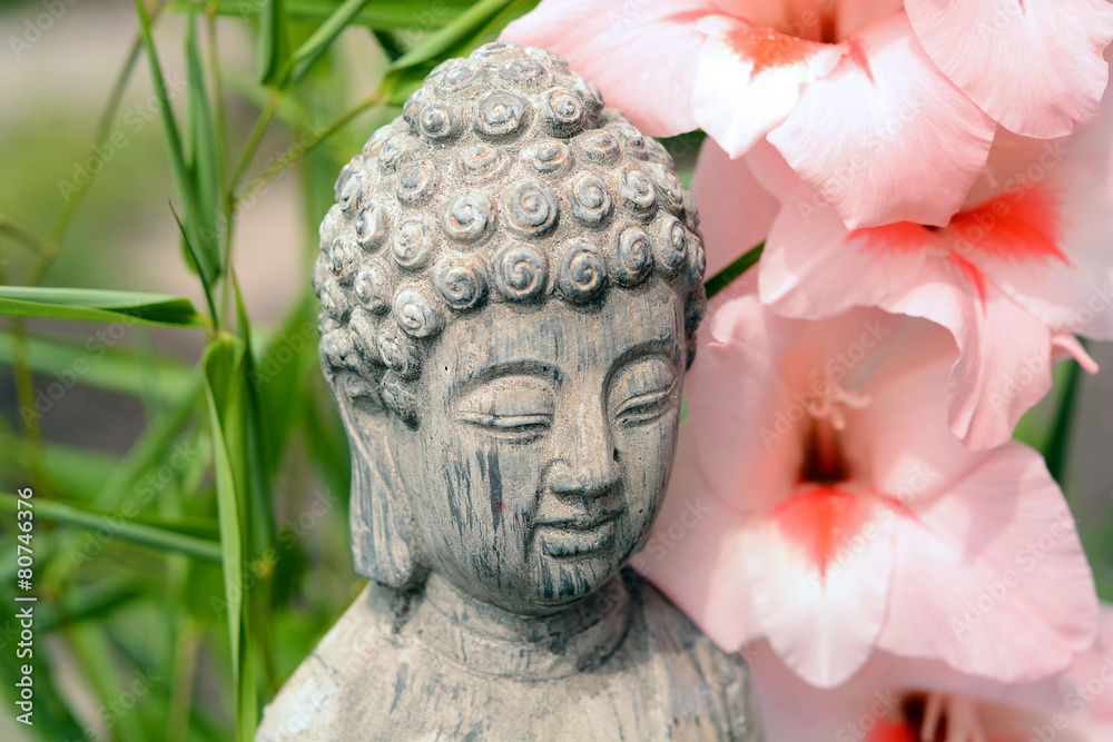 Obraz premium Grey buddha statue in flower garden with bamboo