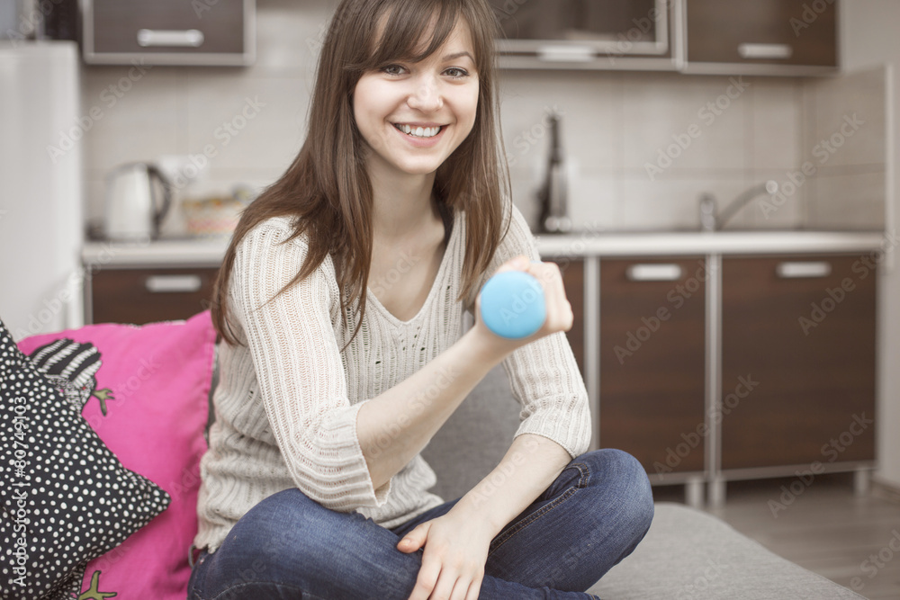 Fototapeta premium Smiling woman exercising with hantel on sofa