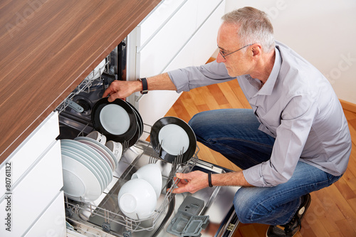 Senior man in kitchen, empty out the dishwasher 3 photo