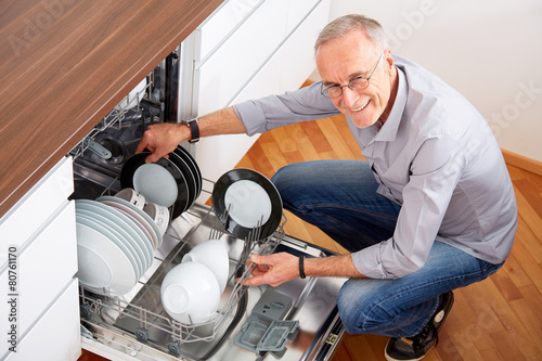 Senior man in kitchen, empty out the dishwasher 2 photo