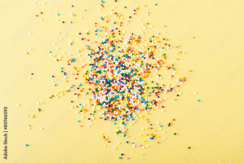 Colorful round sprinkles spilled on yellow background, isolated