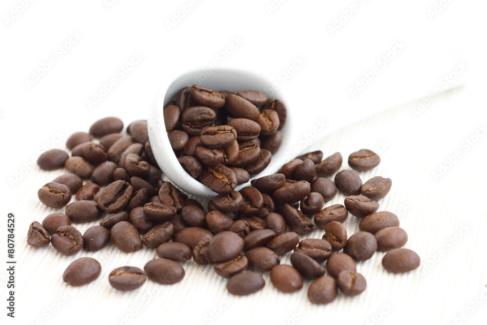 Fototapeta premium Roasted coffee beans in ceramic measuring scoop. On fabric.
