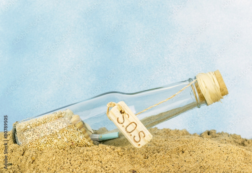 A glass bottle with SOS in sand on a blue background A glass bottle with SOS in sand on a blue background