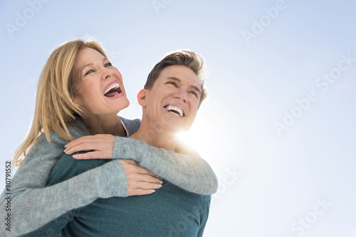 Man Giving Piggyback Ride To Woman Against Clear Sky