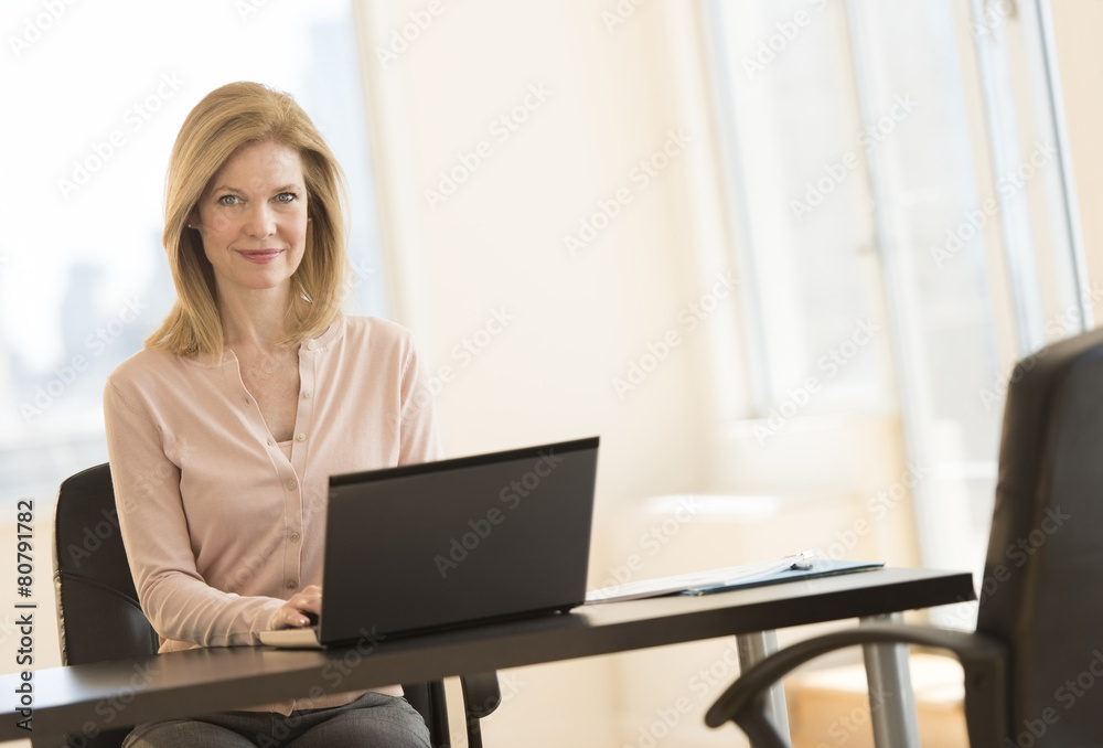 Businesswoman Using Laptop At Desk In Office Businesswoman Using Laptop At Desk In Office