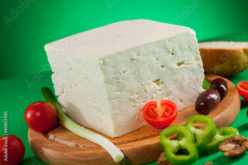 White feta cheese on wooden board and green background