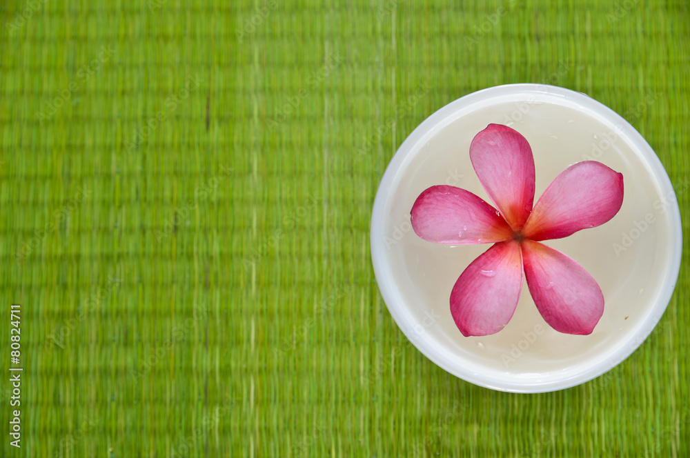 Red frangipani flower in glass bowl on straw mat Red frangipani flower in glass bowl on straw mat
