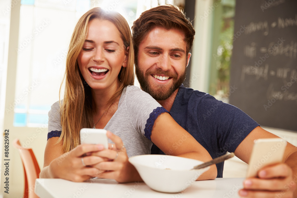Young Couple Eating Breakfast Whilst Using Mobile Phones Young Couple Eating Breakfast Whilst Using Mobile Phones
