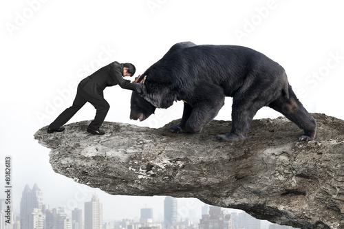 Businessman fighting against black bear on cliff with sky citysc