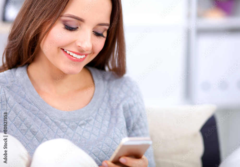 Pretty girl using her smartphone on couch at home in the living Pretty girl using her smartphone on couch at home in the living