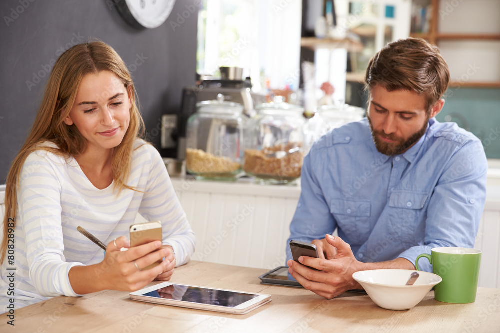 Young Couple Eating Breakfast Whilst Using Mobile Phones Young Couple Eating Breakfast Whilst Using Mobile Phones