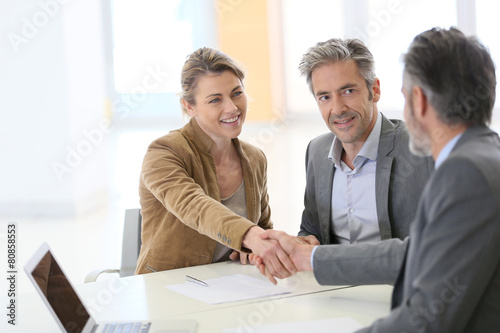 Obraz na plátně Couple in bank office shaking hand to financial adviser
