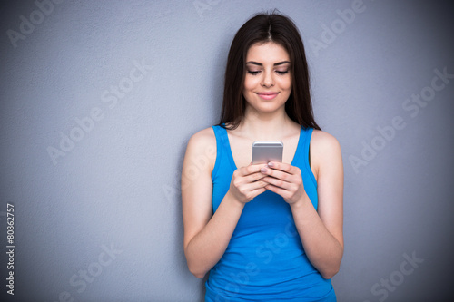 Smiling woman using smartphone over gray background