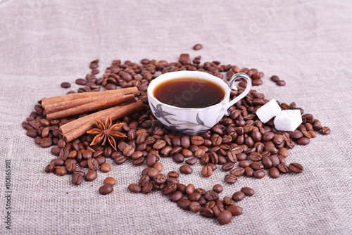 Cup of coffee with coffee beans, sugar, cinnamon on linen table
