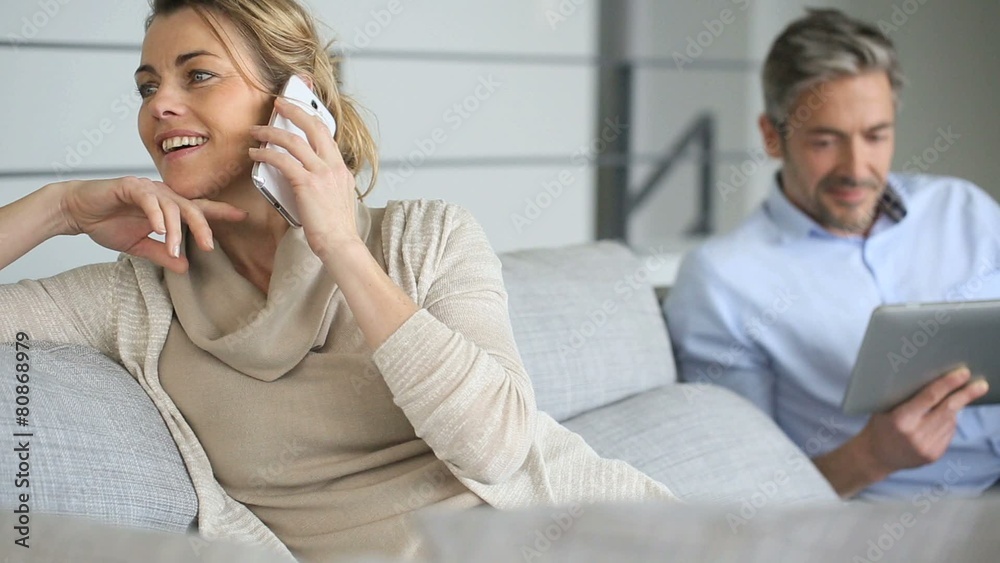 Mature woman talking on smartphone, husband using tablet Mature woman talking on smartphone, husband using tablet