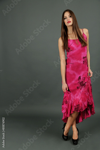 Beautiful young woman in long pink dress on dark gray background